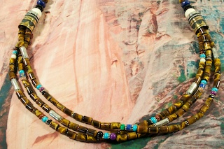 Genuine Assorted Gemstones Necklace with Sterling Silver and Gold Filled Barrels. Featuring Genuine Tiger's Eye with Genuine Turquoise, Sugilite, Blue Lapis and Black Onyx Accents. Sterling Silver Cones and Clasp. Stunning Necklace Created by Navajo Artist Tommy Singer. Signed.